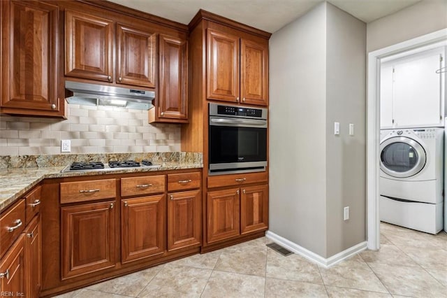 kitchen featuring decorative backsplash, appliances with stainless steel finishes, light stone counters, light tile patterned floors, and washer / dryer