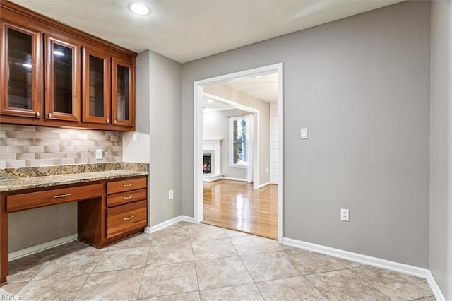 kitchen with decorative backsplash, light tile patterned floors, built in desk, and light stone counters