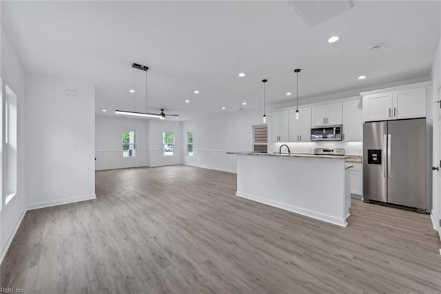 kitchen featuring stainless steel appliances, ceiling fan, a kitchen island with sink, white cabinetry, and hanging light fixtures