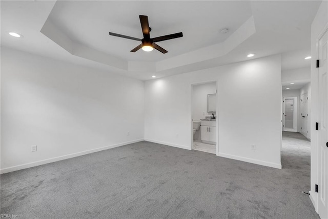 carpeted spare room with a tray ceiling, ceiling fan, and sink