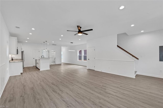 unfurnished living room with light wood-type flooring, electric panel, and ceiling fan