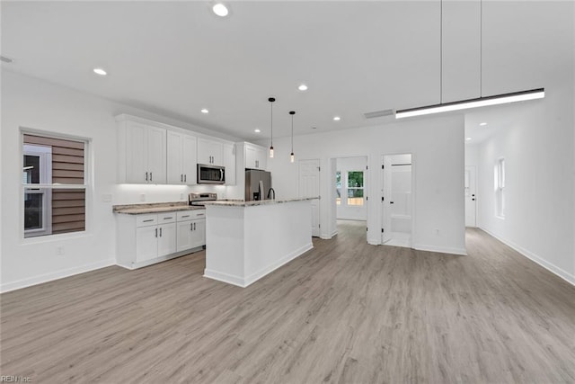 kitchen featuring appliances with stainless steel finishes, pendant lighting, white cabinets, light hardwood / wood-style floors, and an island with sink