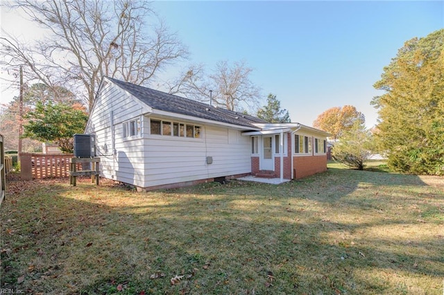 rear view of house with central AC unit and a lawn