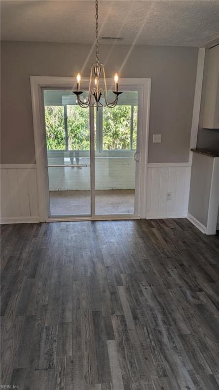 unfurnished dining area with dark hardwood / wood-style flooring, a textured ceiling, and a chandelier