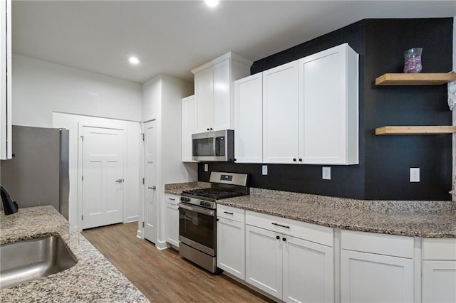 kitchen featuring light stone countertops, appliances with stainless steel finishes, sink, light hardwood / wood-style floors, and white cabinetry