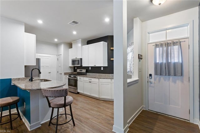 kitchen with light stone countertops, appliances with stainless steel finishes, sink, white cabinets, and hardwood / wood-style floors