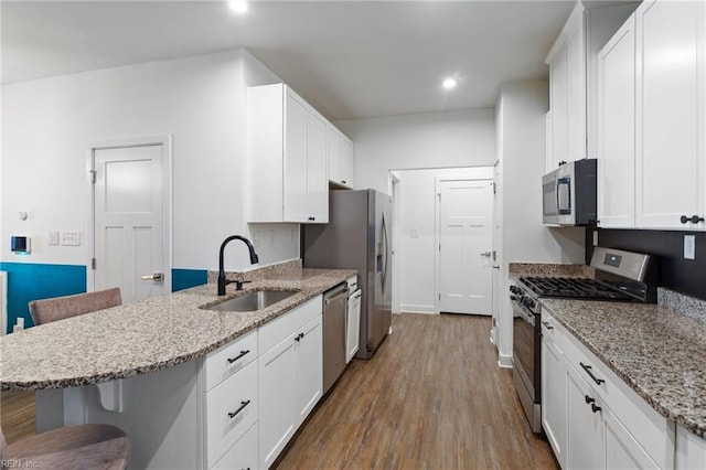 kitchen featuring sink, hardwood / wood-style floors, a kitchen bar, white cabinets, and appliances with stainless steel finishes