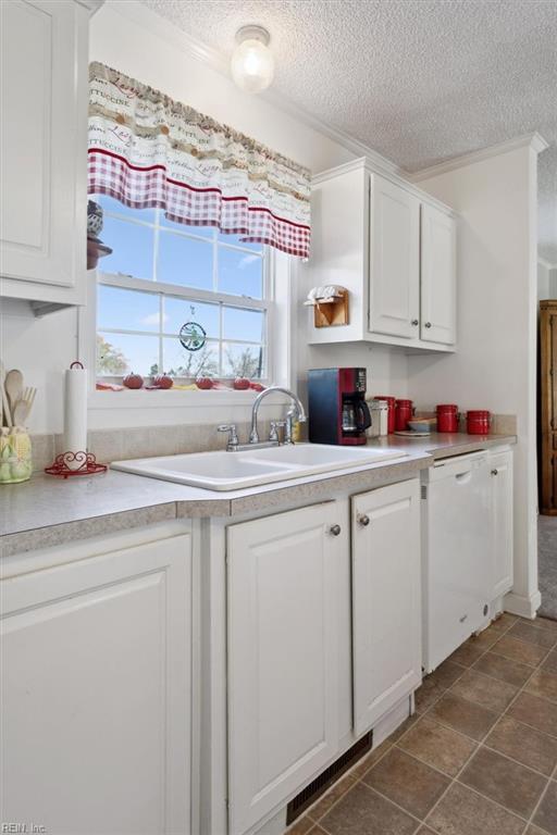 kitchen with white dishwasher, white cabinets, dark tile patterned floors, and a textured ceiling