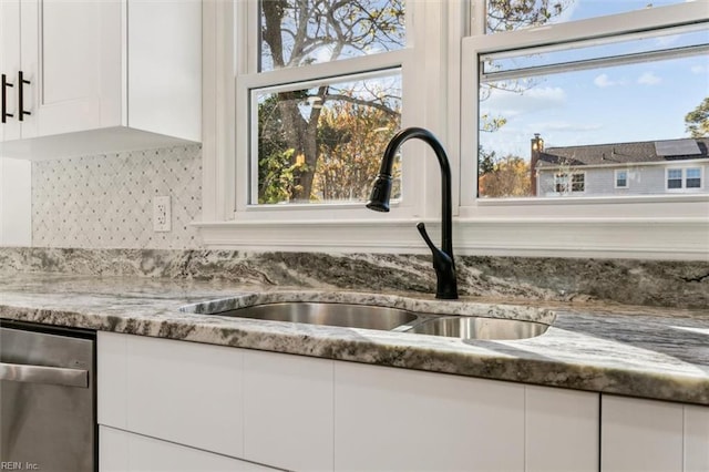 room details featuring stainless steel dishwasher, white cabinetry, sink, and dark stone counters