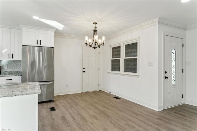 kitchen featuring crown molding, hardwood / wood-style flooring, stainless steel fridge, light stone countertops, and white cabinetry