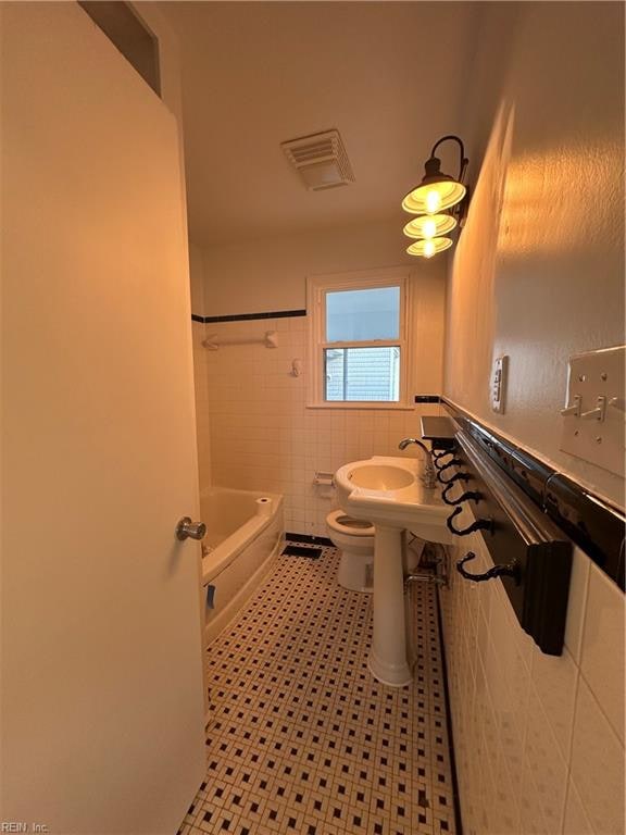 full bathroom featuring sink, washtub / shower combination, tile walls, and toilet