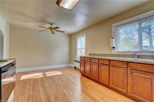 kitchen featuring light wood-type flooring, stainless steel range, ceiling fan, sink, and radiator heating unit