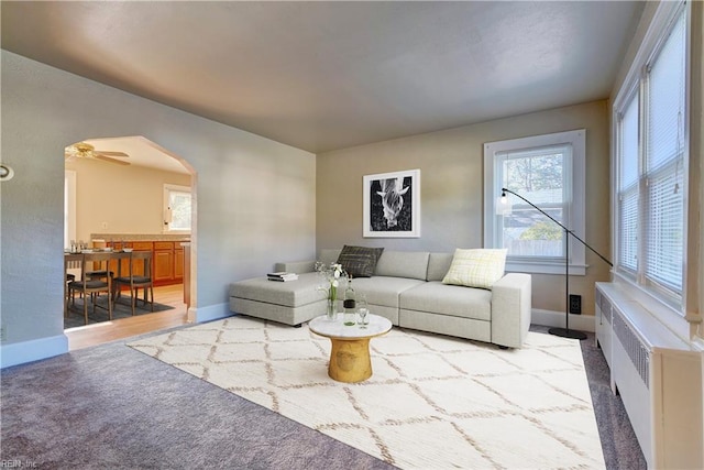 carpeted living room with ceiling fan and radiator