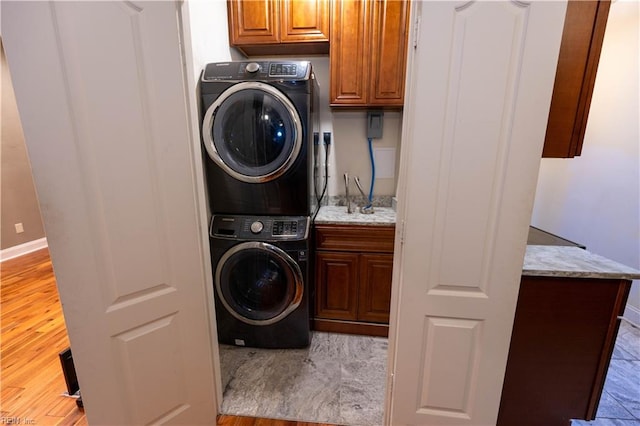 laundry room featuring stacked washing maching and dryer, cabinets, and light hardwood / wood-style floors