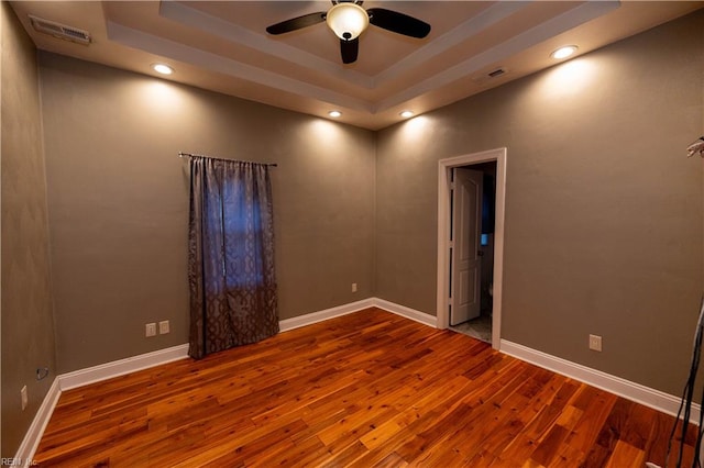 empty room featuring a raised ceiling, ceiling fan, and hardwood / wood-style flooring