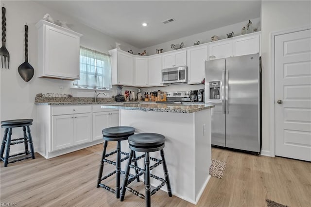 kitchen with a breakfast bar area, white cabinetry, light hardwood / wood-style flooring, and stainless steel appliances