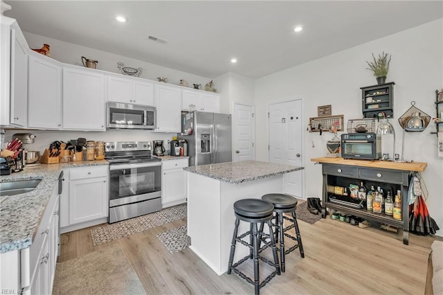 kitchen with a center island, light stone counters, light hardwood / wood-style flooring, white cabinets, and appliances with stainless steel finishes