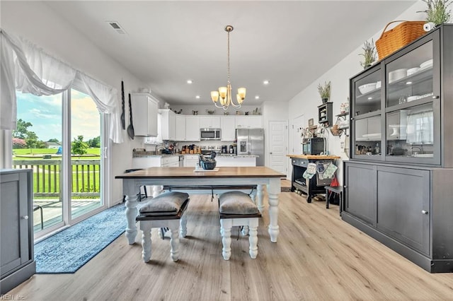 kitchen with white cabinets, appliances with stainless steel finishes, light hardwood / wood-style floors, and a chandelier