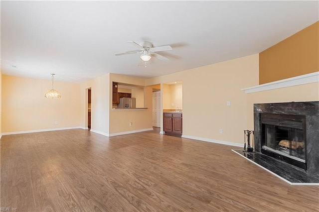 unfurnished living room featuring wood finished floors, ceiling fan with notable chandelier, baseboards, and a premium fireplace