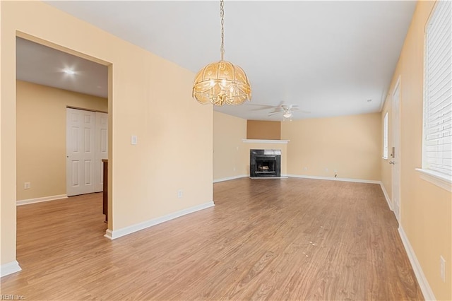 unfurnished living room featuring a high end fireplace, ceiling fan with notable chandelier, light wood finished floors, and baseboards