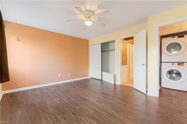 unfurnished bedroom featuring a closet, stacked washer and clothes dryer, baseboards, and dark wood-style flooring