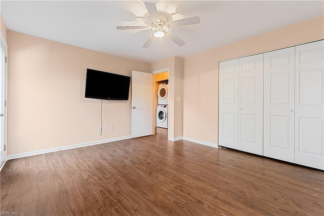 unfurnished bedroom with hardwood / wood-style floors, a closet, stacked washer / dryer, and ceiling fan