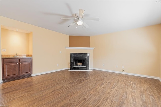 unfurnished living room with ceiling fan, wood-type flooring, sink, and a premium fireplace