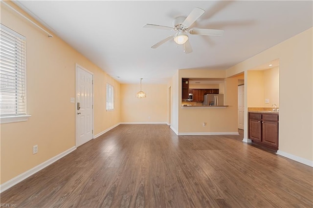 unfurnished living room with a ceiling fan, dark wood-style floors, baseboards, and a sink