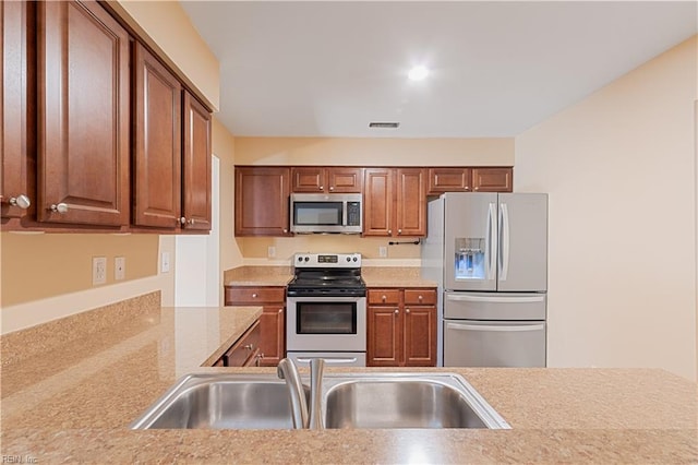 kitchen featuring light countertops, brown cabinetry, appliances with stainless steel finishes, and a sink