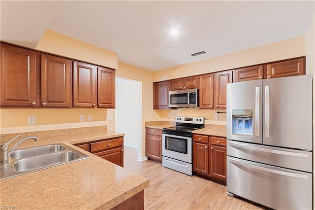 kitchen with a sink, stainless steel appliances, light wood-style flooring, and light countertops