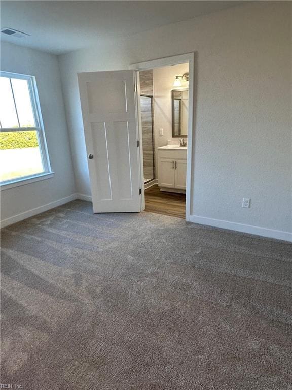 unfurnished bedroom featuring ensuite bath and dark colored carpet