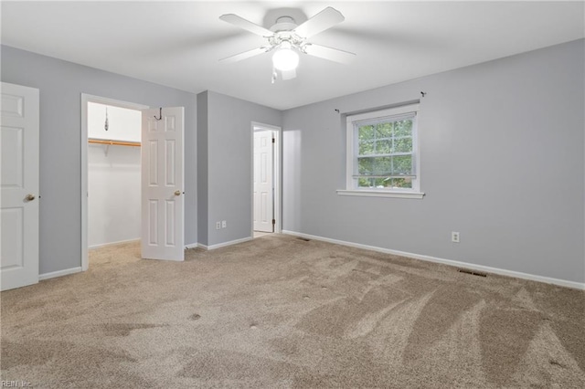 unfurnished bedroom with a walk in closet, carpet floors, a closet, and ceiling fan