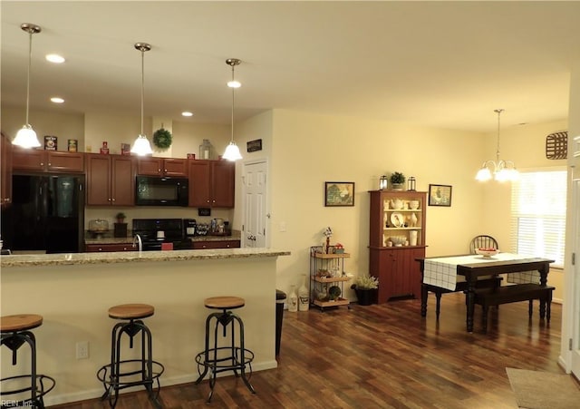 kitchen featuring light stone countertops, dark hardwood / wood-style floors, decorative light fixtures, a breakfast bar, and black appliances