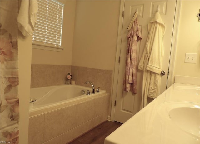 bathroom with hardwood / wood-style floors, vanity, and tiled bath