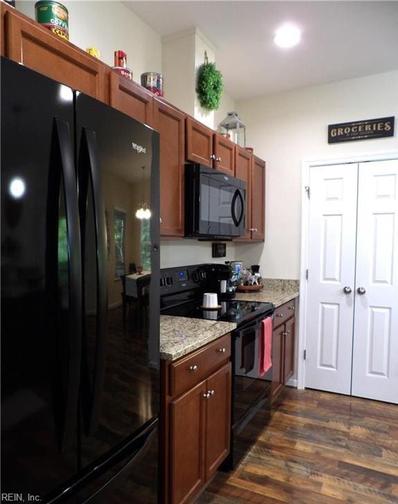 kitchen featuring a chandelier, dark hardwood / wood-style floors, light stone counters, and black appliances