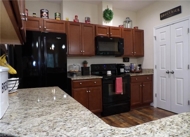 kitchen with light stone countertops, dark wood-type flooring, and black appliances