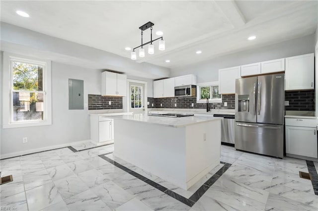 kitchen with decorative backsplash, appliances with stainless steel finishes, a kitchen island, pendant lighting, and white cabinetry