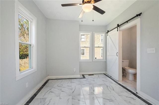 unfurnished bedroom with ceiling fan, a barn door, and connected bathroom