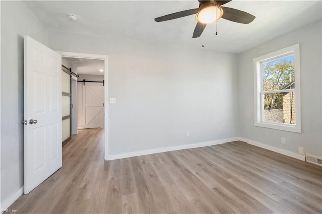 spare room with ceiling fan, a barn door, and light wood-type flooring