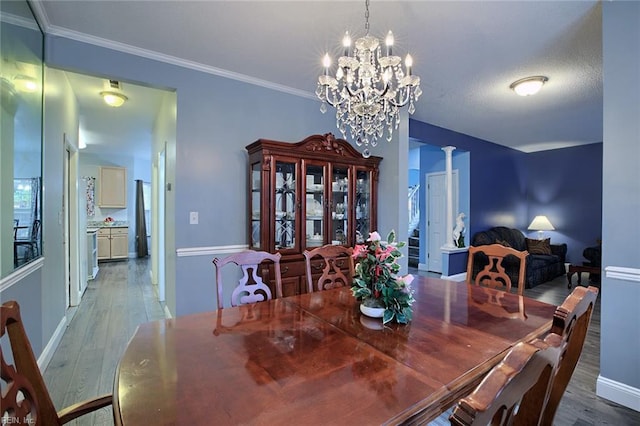 dining area with a chandelier, hardwood / wood-style floors, decorative columns, and ornamental molding