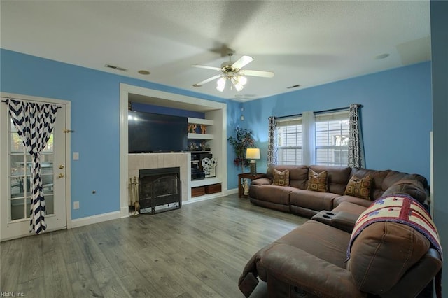 living room with hardwood / wood-style floors, ceiling fan, a tiled fireplace, and built in shelves