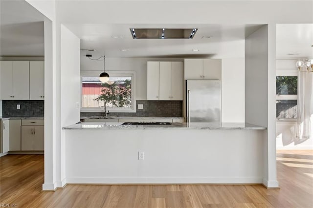 kitchen featuring stainless steel built in refrigerator, light wood-type flooring, light stone counters, and backsplash