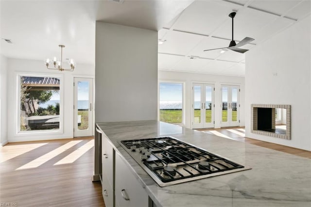 kitchen with light stone countertops, ceiling fan with notable chandelier, stainless steel gas cooktop, hardwood / wood-style floors, and hanging light fixtures