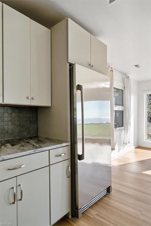 kitchen with white cabinets, stainless steel fridge, light wood-type flooring, and backsplash