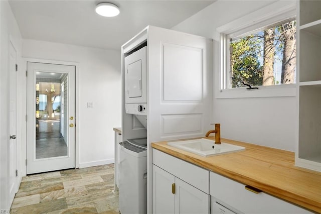 clothes washing area with sink, cabinets, and stacked washer and clothes dryer