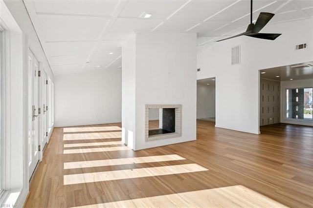 unfurnished living room with ceiling fan, a high ceiling, and light wood-type flooring