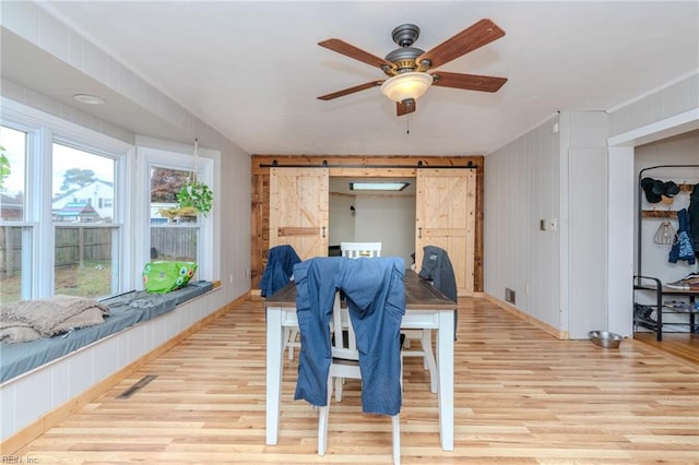 interior space featuring ceiling fan, a barn door, wooden walls, and light hardwood / wood-style flooring