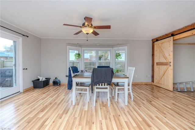 dining space with a barn door, ceiling fan, ornamental molding, and light wood-type flooring