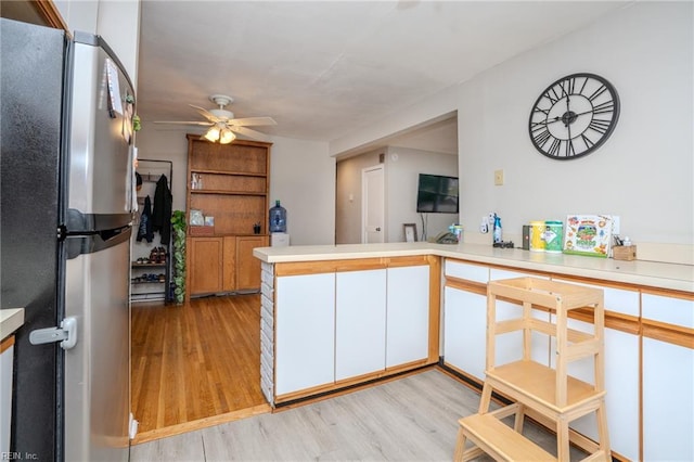 kitchen featuring white cabinets, light hardwood / wood-style flooring, ceiling fan, stainless steel fridge, and kitchen peninsula