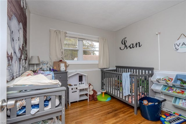 bedroom with wood-type flooring and a nursery area